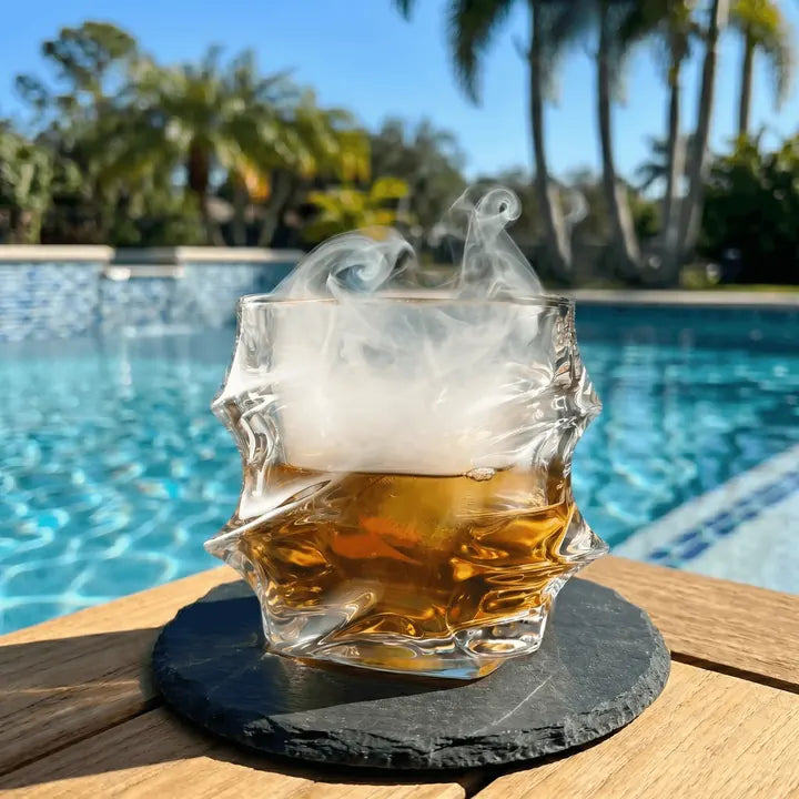 Smoke-filled Storm glass of whisky on a slate coaster by a pool