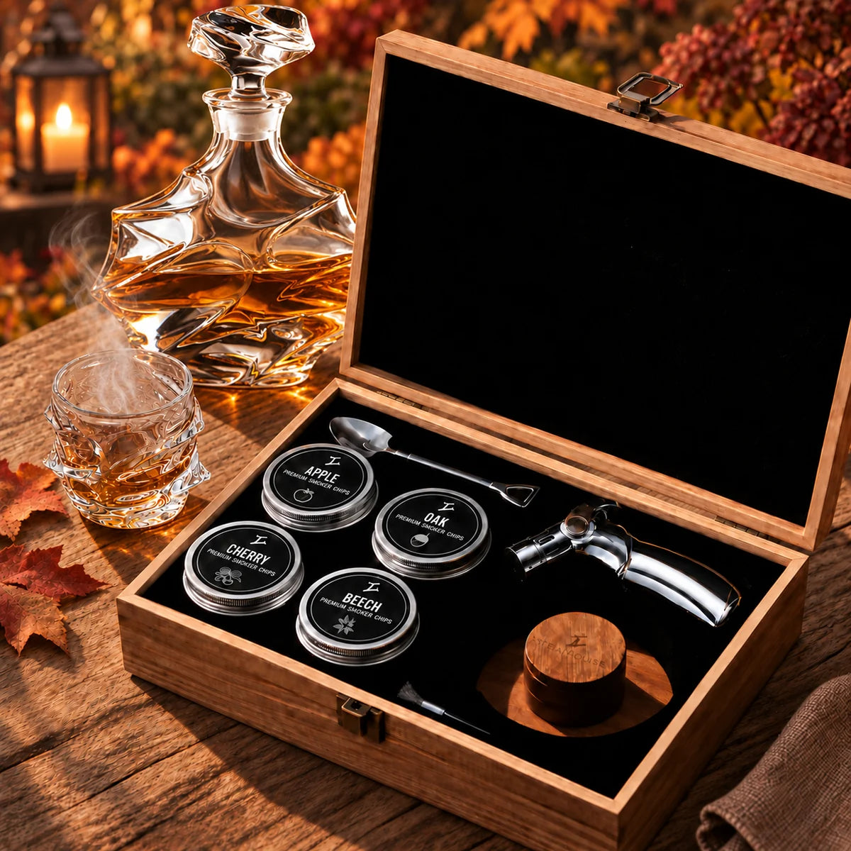 A cocktail smoker kit in an open wooden box next to a decanter and a smoking glass of whiskey.