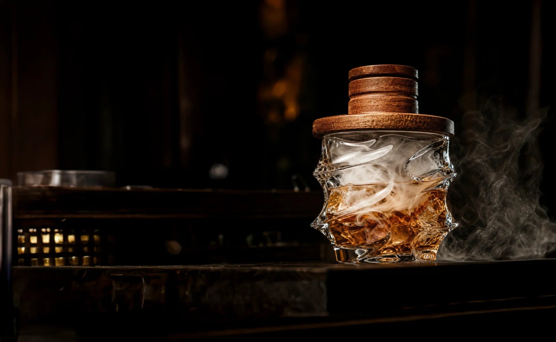 Storm whisky glass with a wooden smoker lid and aromatic smoke on a dark bar